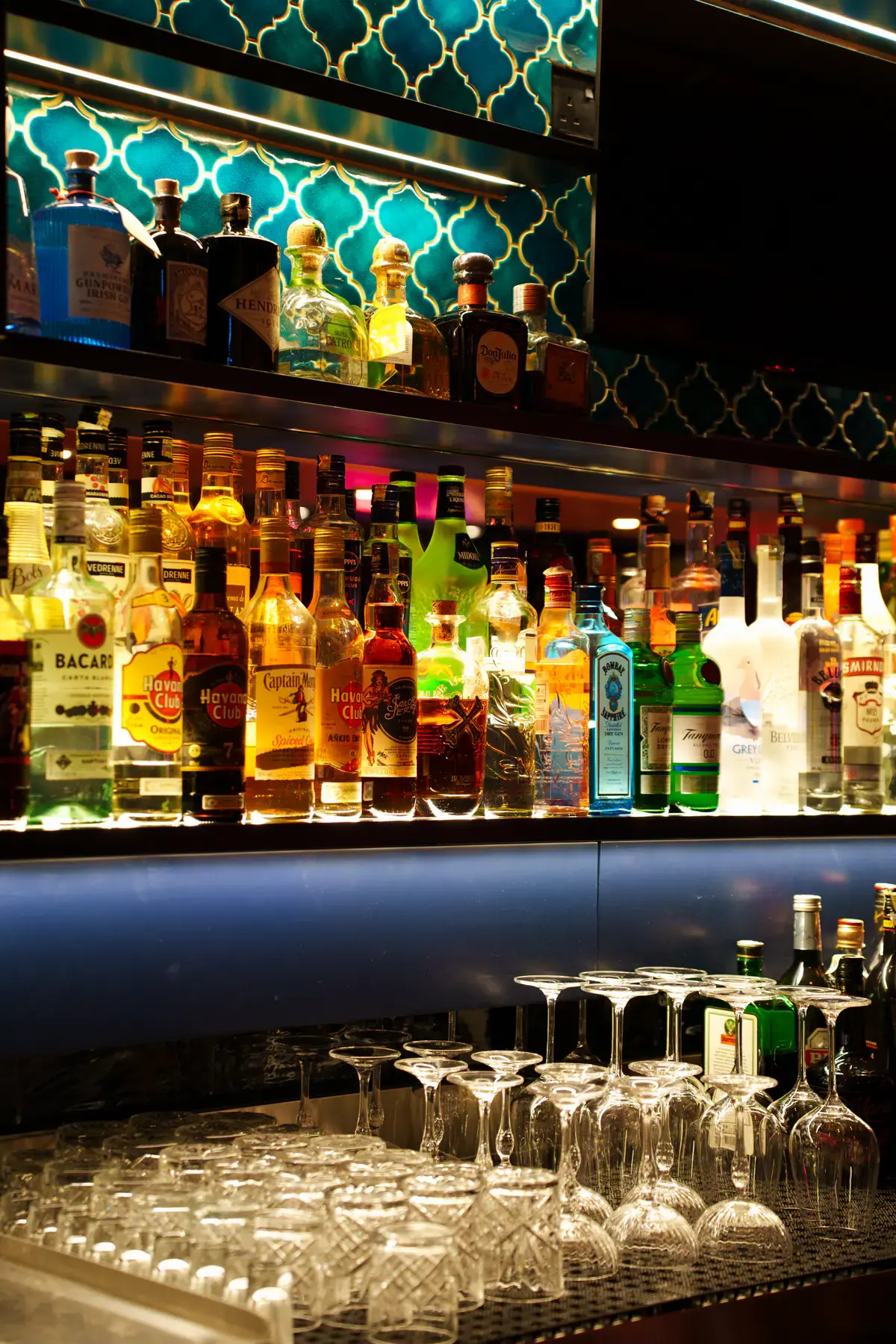 The back bar lined with spirits and glassware under teal tiles
