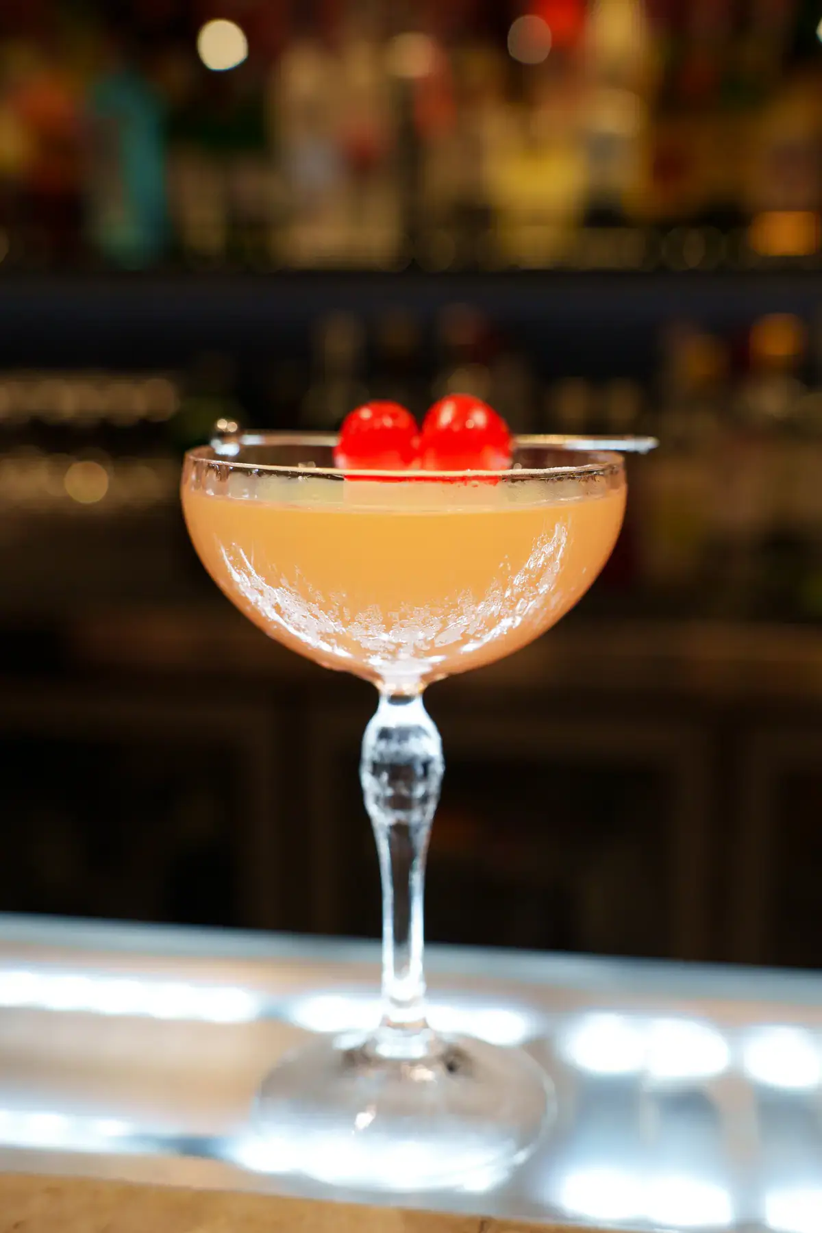 A coupe cocktail garnished with cherries on the bar