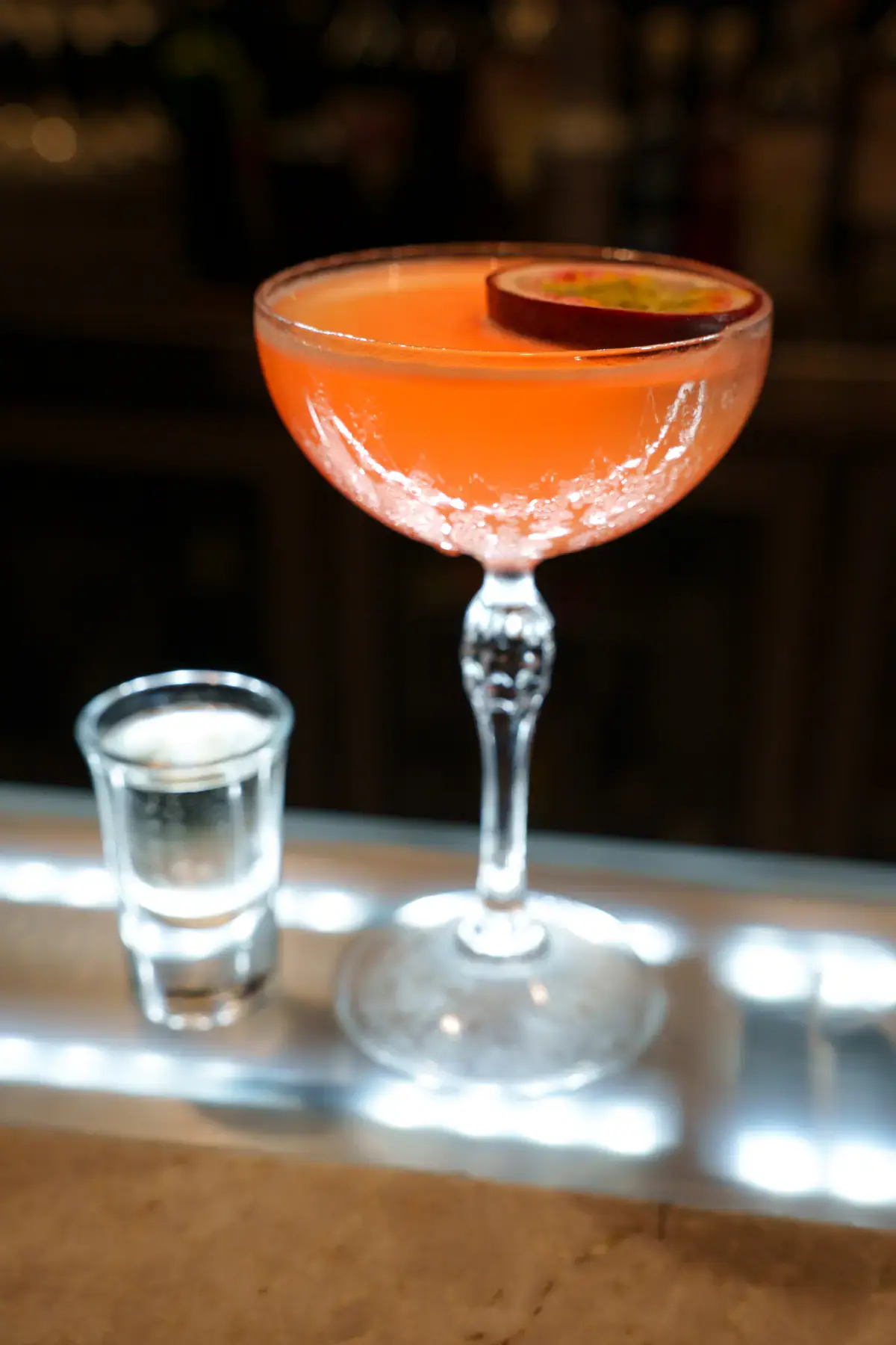 A passion fruit cocktail in a coupe with a shot on the side