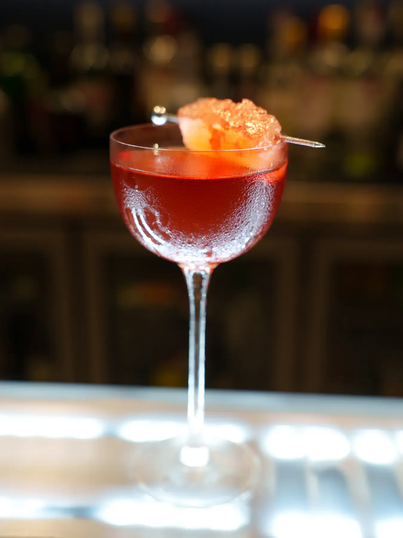 A ruby-red cocktail in a stemmed glass with a citrus garnish