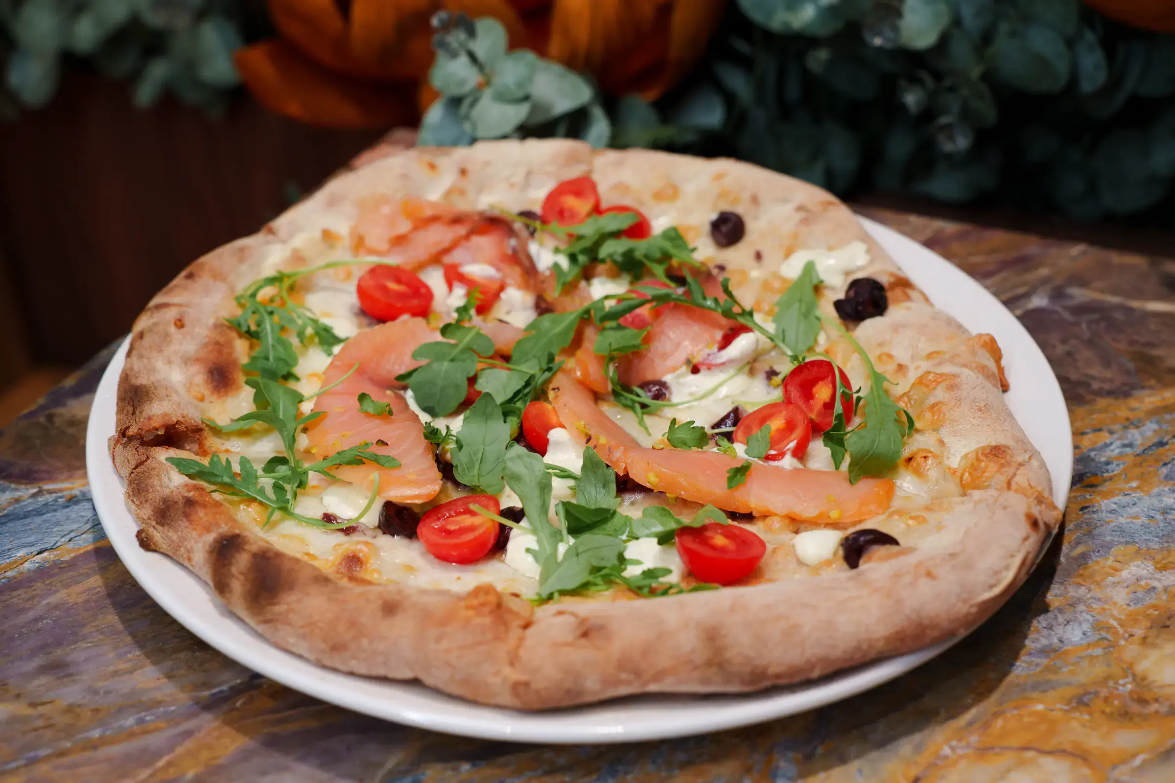 Smoked salmon pizza with rucola, cherry tomatoes and olives